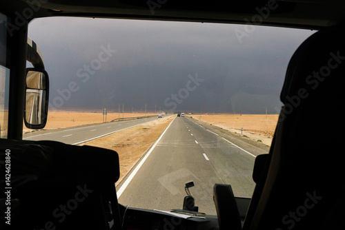 Obraz na płótnie Desert road view from bus. Stormy sky horizon. Travel in Morocco. Long straight highway. Empty sandy landscape. Dramatic road trip. Adventure drive. Transport journey. Asphalt desert route. w salonie