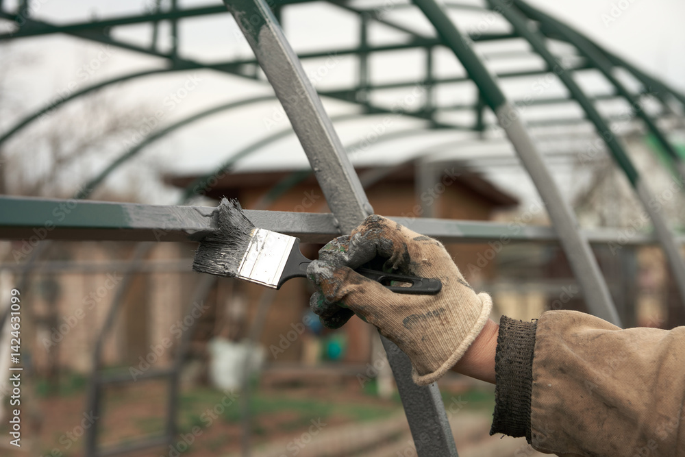 Anticorrosive coating of the metal structure. A man's hand is painting the frame of a greenhouse with a brush. Close-up.