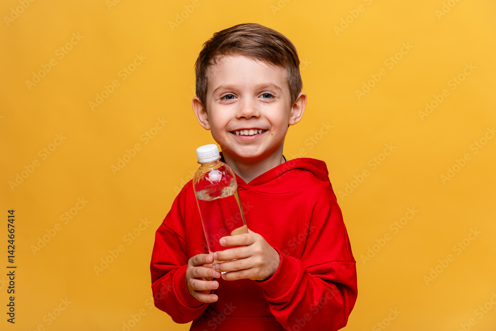 A happy little boy drinks water for health on yellow background. The child is holding a water bottle. A kid with a plastic bottle. Children's activity and energy, generation Z. body hydration concept