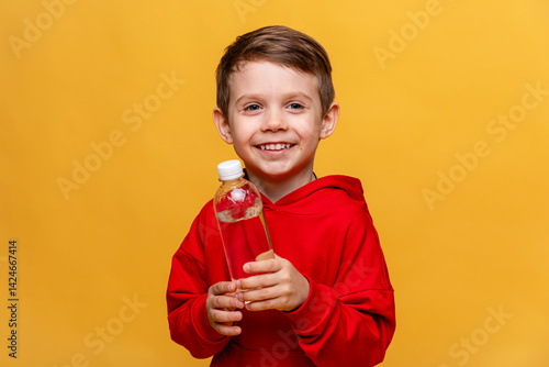 Obraz na płótnie A happy little boy drinks water for health on yellow background. The child is holding a water bottle. A kid with a plastic bottle. Children's activity and energy, generation Z. body hydration concept w salonie