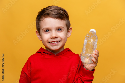 Obraz na płótnie A happy little boy drinks water for health on yellow background. The child is holding a water bottle. A kid with a plastic bottle. Children's activity and energy, generation Z. body hydration concept w salonie