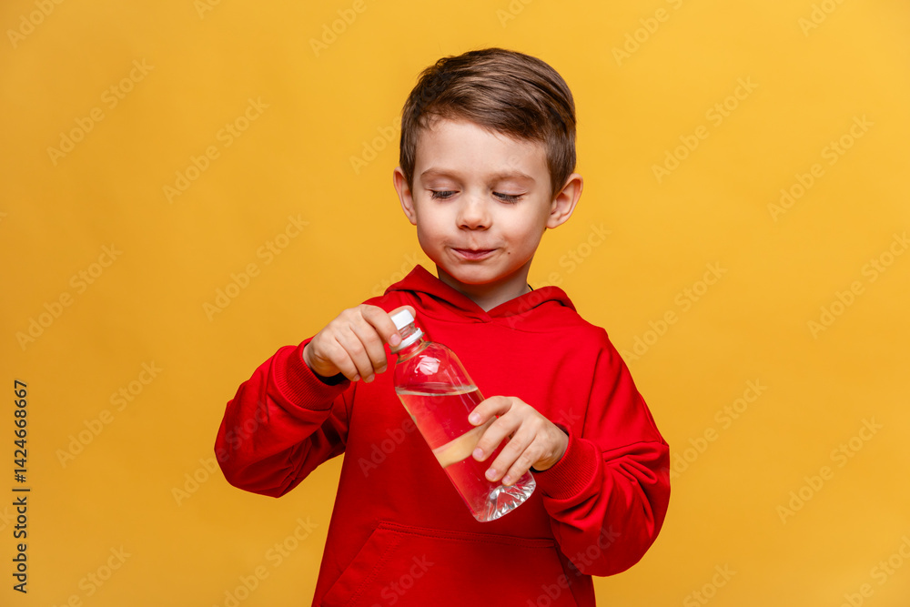 Happy little boy drinks water for health on yellow background. The child is opening a bottle of water. A kid with a plastic bottle. Children's activity and energy, generation Z. body hydration concept