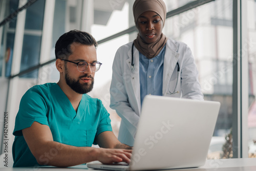 Doctors using laptop in hospital discuss patient records