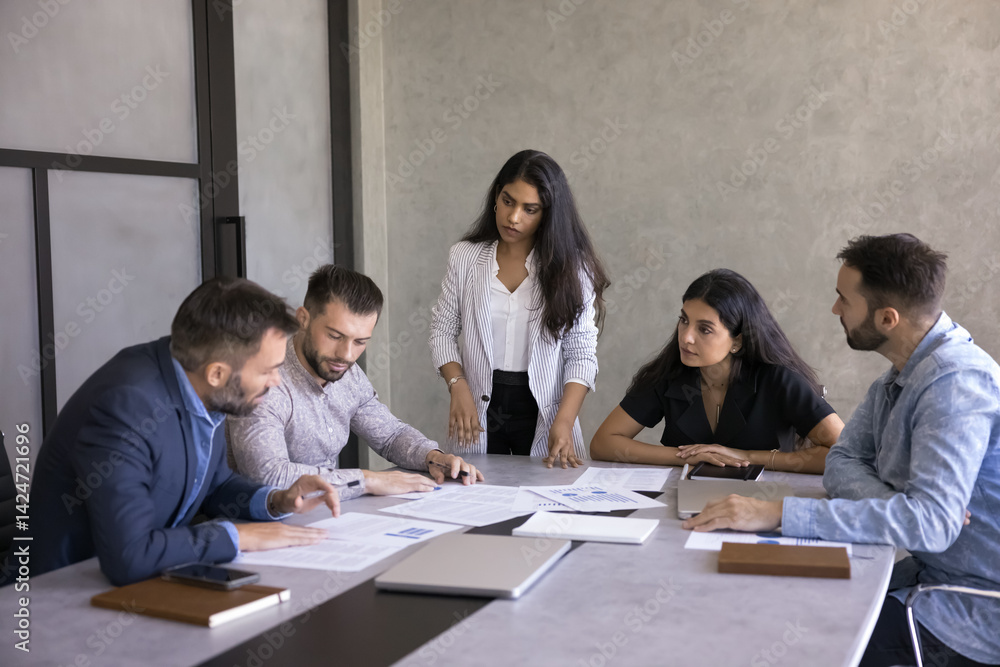 Fototapeta premium Group of five professionals engaged in brainstorming or decision-making, take part in collaborative meeting seated around conference table, discuss documents, charts, and report, review paperwork data