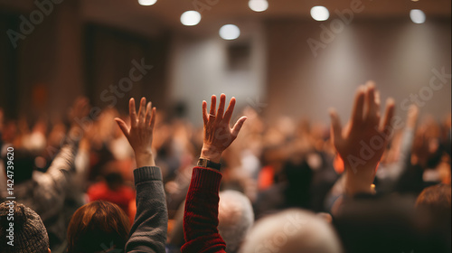 Engaged audience raises hands in a meeting.  Diverse participants at an event in an indoor auditorium.  Active participation shown.