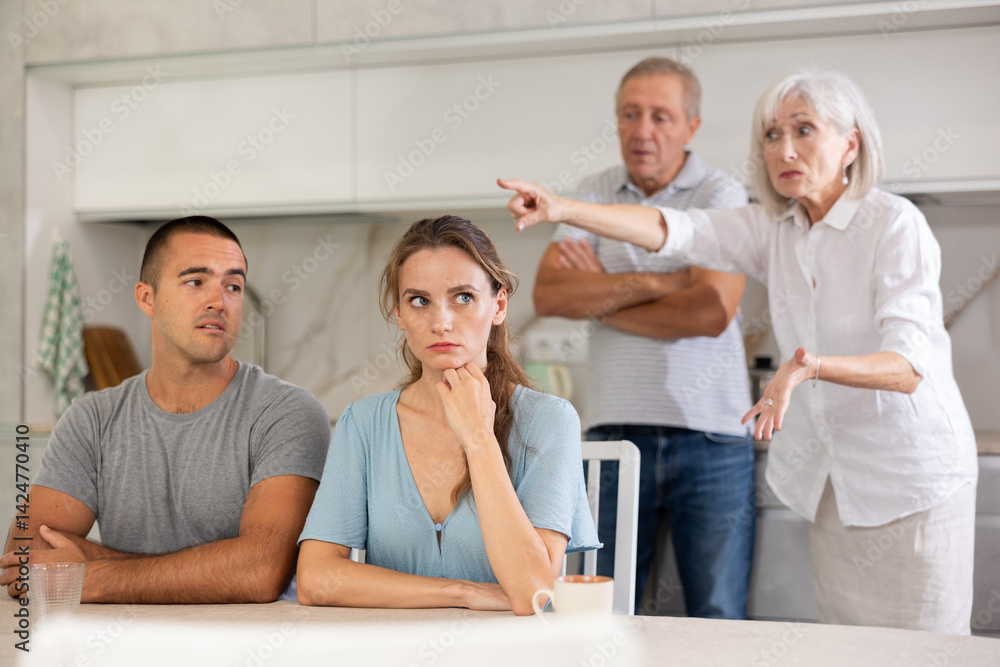 Fototapeta premium Elderly parents make claims to young couple in home kitchen