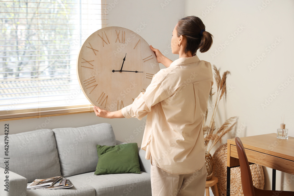 Young woman holding clock near sofa in living room