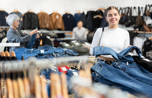 Obraz na płótnie Glad young female customer looking at jean trousers put on stand in clothes store w salonie
