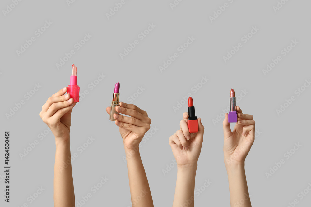 Female hands with many lipsticks on grey background