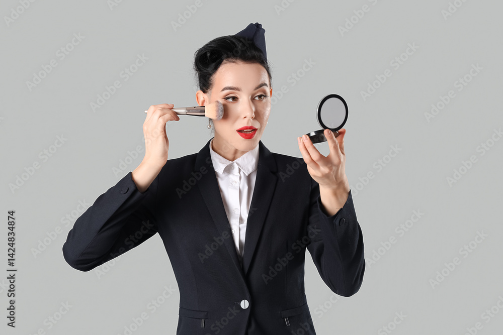 Young pin-up stewardess applying makeup powder on light background