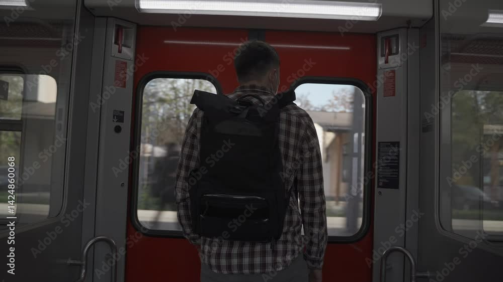 Man wearing backpack and shirt stands facing away near sliding doors of S-Bahn train in Munich, Germany. He waits for his stop to get off, depicting daily commuting in city public transport network. Man wearing backpack and shirt stands facing away near sliding doors of S-Bahn train in Munich, Germany. He waits for his stop to get off, depicting daily commuting in city public transport network.