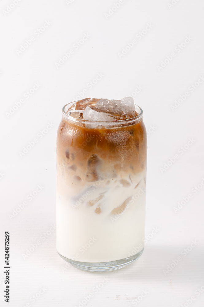 A glass of coffee with ice in it. The coffee is a light brown color and the ice is white A glass of coffee with ice in it. The coffee is a light brown color and the ice is white