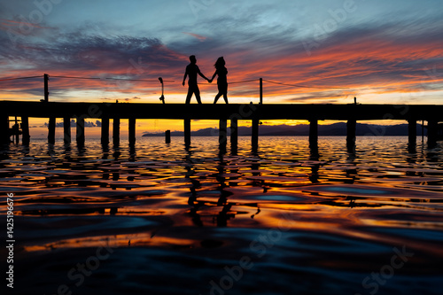 Obraz na płótnie The image shows a silhouette of a couple holding hands and walking on a pier at sunset w salonie