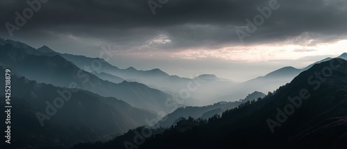 Misty mountain landscape at dusk, showcasing layers of rolling hills and dramatic cloud formations.