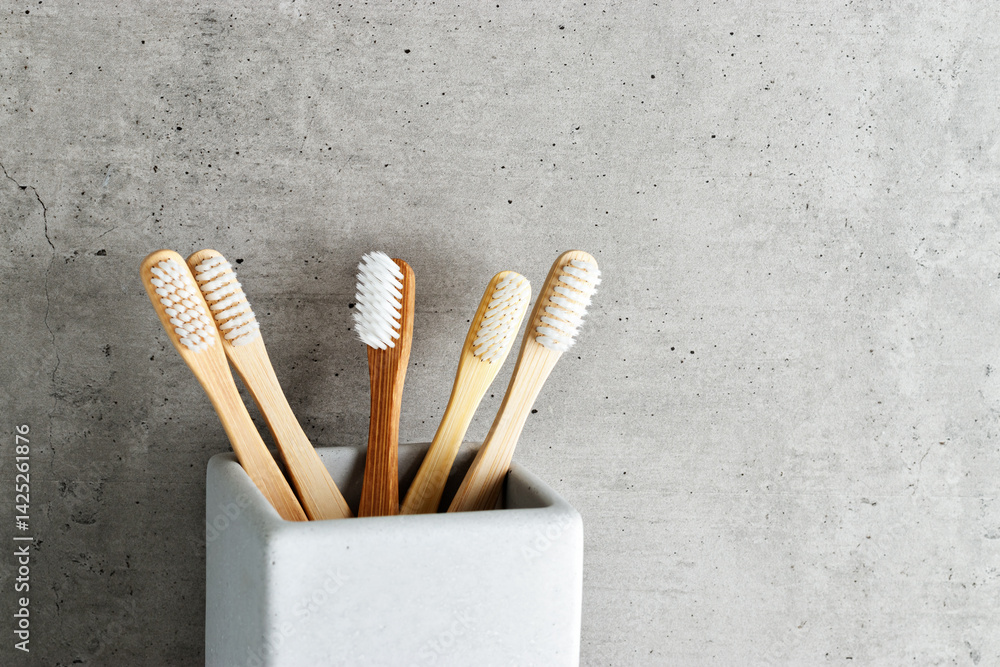 Eco-friendly wood toothbrushes with soft white bristles in modern grey concrete holder. Minimal bathroom design, sustainable hygiene concept, Neutral tones, zerowaste lifestyle, eco-conscious living