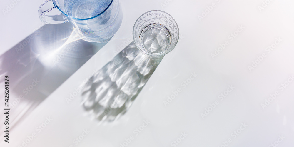 Water Glass with shadows at sunlight on white, delicate purple blue color, minimal aesthetic top view shiny glasses at natural light, summer drink concept, pastel gradient interplay light and shadow