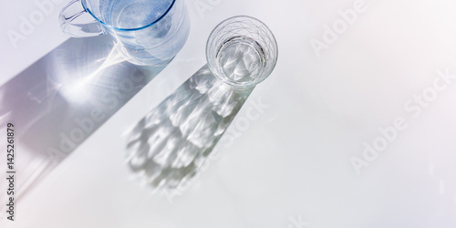 Obraz na płótnie Water Glass with shadows at sunlight on white, delicate purple blue color, minimal aesthetic top view shiny glasses at natural light, summer drink concept, pastel gradient interplay light and shadow w salonie