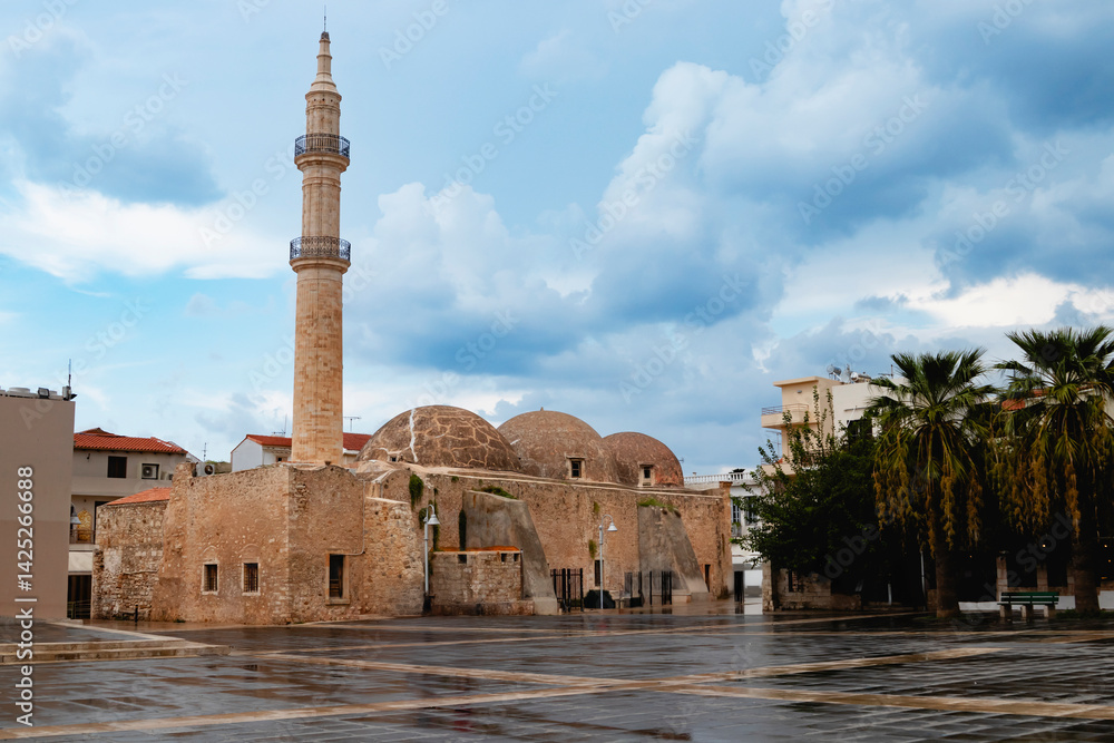 A captivating view of a historic mosque featuring a tall minaret in Rethymno, Greece, against a cloudy sky. Crete island.