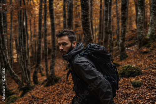 Obraz na płótnie The image shows a man hiking in a forest during autumn, wearing a backpack and a jacket, surrounded by trees with brown leaves on the ground w salonie
