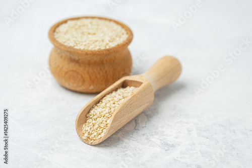 Natural sesame seeds in wooden scoop and jar on light countertop