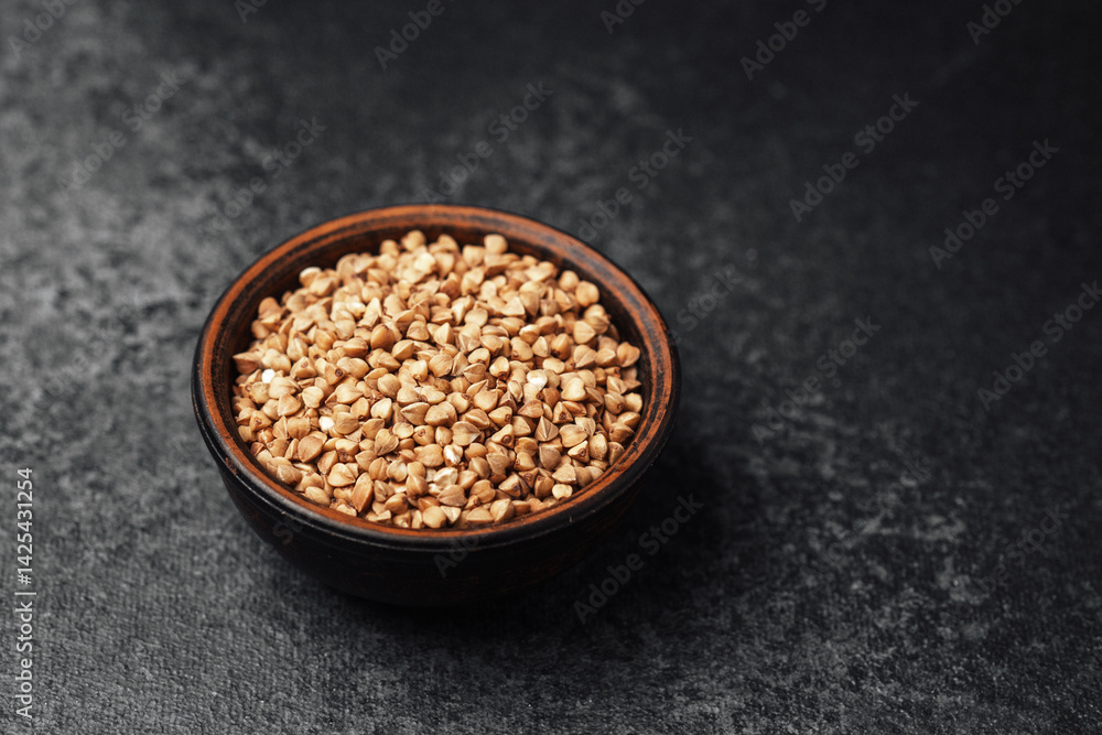 Buckwheat seeds in a bowl on a dark surface with natural lighting Buckwheat seeds in a bowl on a dark surface with natural lighting