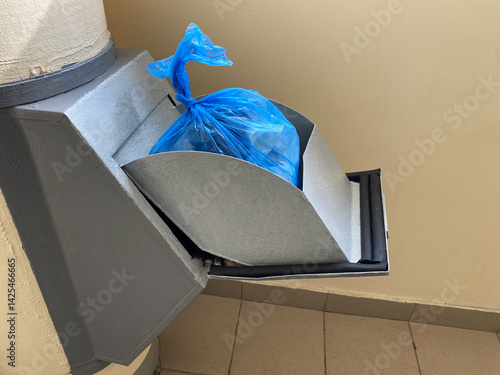 Blue disposable plastic bag of trash in the manhole door of the garbage chute indoor entrance of an apartment building. Convenient waste collection system