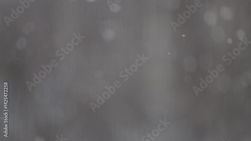 Light snow swirls and falls on a gray background with selective focus and shallow depth of field.