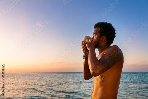 Fijian man blowing traditional conch shell at sunset, Fiji