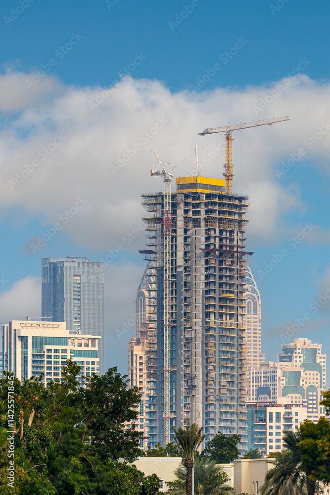 Fototapeta premium Modern Building Under Construction with Red Crane. High-rise building construction site with red tower crane lifting materials