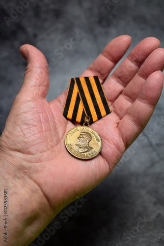 Obraz na plátně Vertical View Of Soviet Medal 'For The Victory Over Germany' With Ribbon Suspension Held In A Person's Palm Against Dark Background