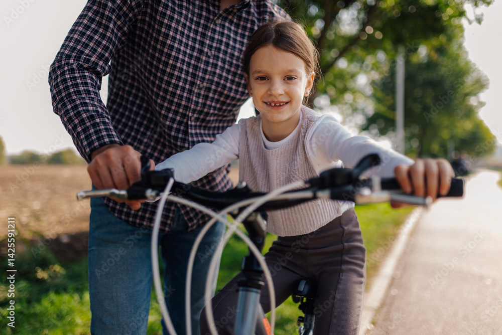 Obraz premium Father helping daughter learning to ride bicycle on a sunny day