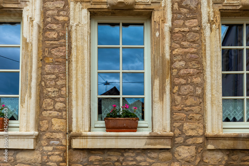 Detailed view of stone building windows with potted flowers on a cloudy day in a quaint village