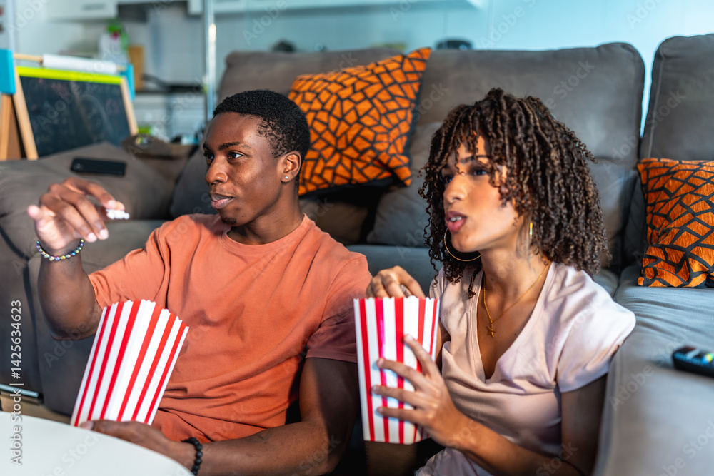 Young couple watching movie and eating popcorn on sofa at home