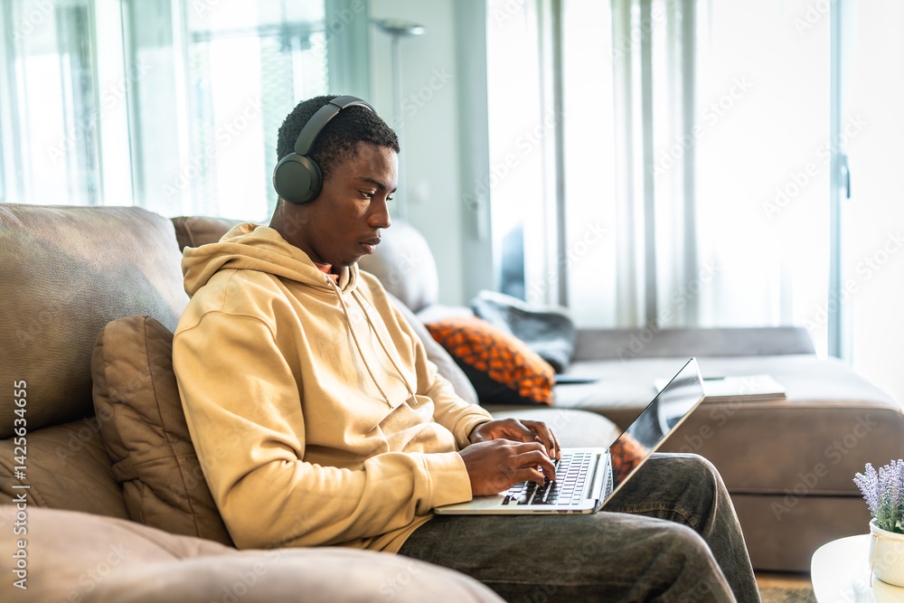 Focused young man working from home using laptop and headphones