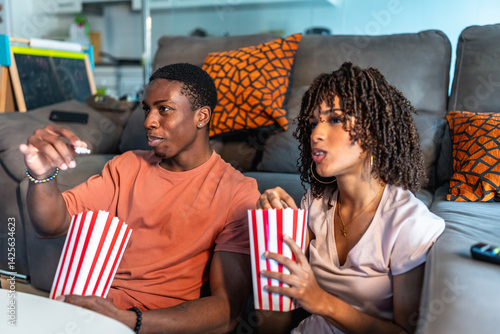 Obraz na płótnie Young couple watching movie and eating popcorn on sofa at home w salonie
