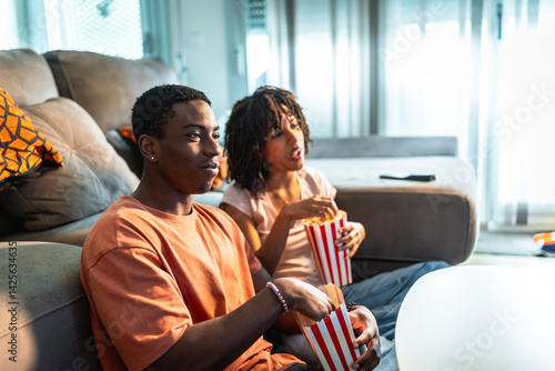 Young couple watching tv and eating popcorn on sofa at home