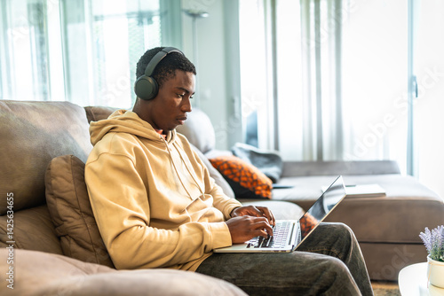 Obraz na płótnie Focused young man working from home using laptop and headphones w salonie