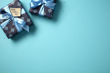 Father's Day gifts flat lay. Two blue gift boxes with ribbons and 'Happy Father's Day' tag on blue background with confetti. Top view, copy space.