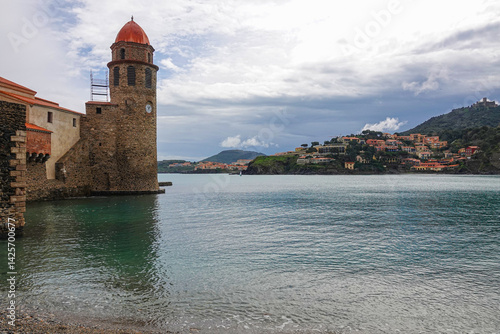 A serene waterfront showcases a historical stone tower with a clock. France, Collioure.