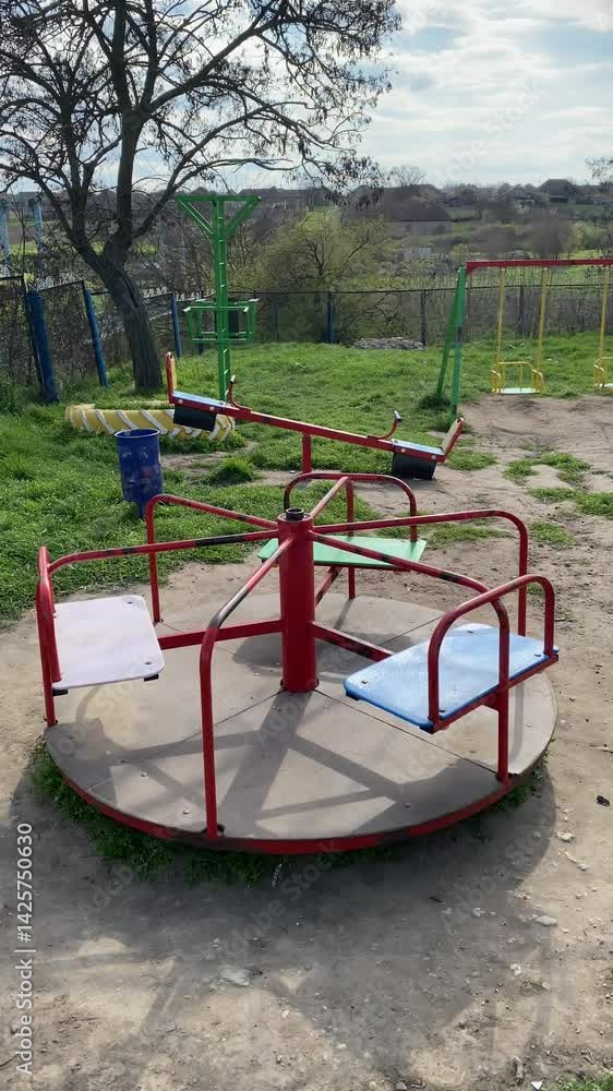 Merry-go-round at local playground with open green space and swings in the background during sunny day Merry-go-round at local playground with open green space and swings in the background during sunny day