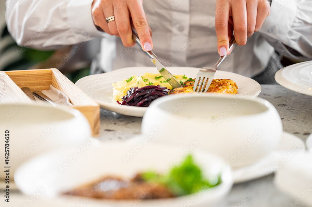 A person elegantly cutting into a plate of food featuring chicken and mashed potatoes, set in a stylish dining environment, highlighting an inviting and enjoyable dining moment. A person elegantly cutting into a plate of food featuring chicken and mashed potatoes, set in a stylish dining environment, highlighting an inviting and enjoyable dining moment.