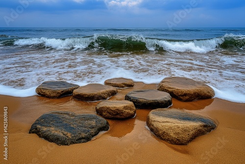 A photograph of rocks on the beach, with waves crashing over them, creating soft water ripples. The tones are predominantly beige, giving the image a cinematic feel