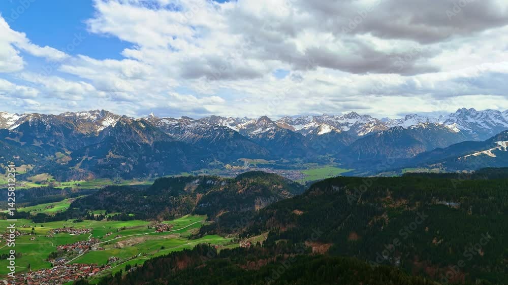 Grey clouds covering the sky over the vast mountainous landscape. Picturesque populated area is siting in the valley among the rocks. Bolsterlang, Bavaria, Germany. Aerial view. Grey clouds covering the sky over the vast mountainous landscape. Picturesque populated area is siting in the valley among the rocks. Bolsterlang, Bavaria, Germany. Aerial view.