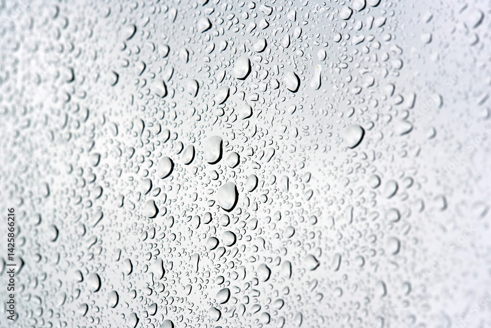 Macro closeup of raindrops scattered across a smooth surface with crystal clear detail showing each droplet's natural shape and texture on calm wet day. Selective focus