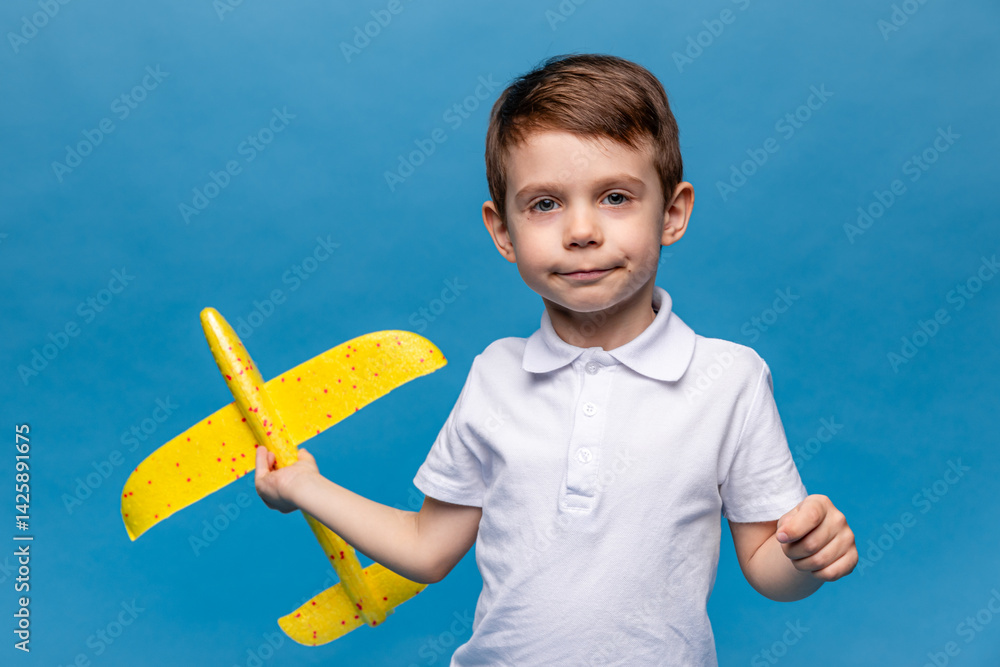 Little boy holding an airplane, playing with a toy airplane. Children's games and imagination. Studio portrait on blue background with copy space. Travel, vacation and dreams of flight concept