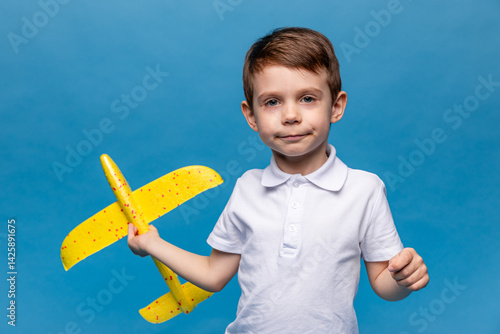 Obraz na płótnie Little boy holding an airplane, playing with a toy airplane. Children's games and imagination. Studio portrait on blue background with copy space. Travel, vacation and dreams of flight concept w salonie