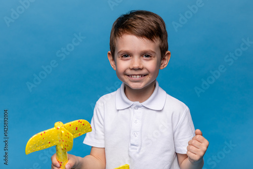 Little boy holding an airplane, playing with a toy airplane. Children's games and imagination. Studio portrait on blue background with copy space. Travel, vacation and dreams of flight concept