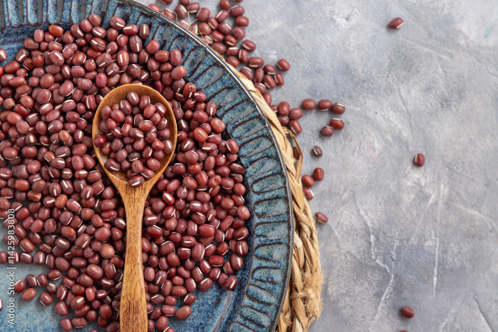Blue plate full of dried red azuki beans with a wooden spoon top view. Vegetarian protein source