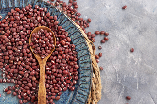 Obraz na płótnie Blue plate full of dried red azuki beans with a wooden spoon top view. Vegetarian protein source w salonie