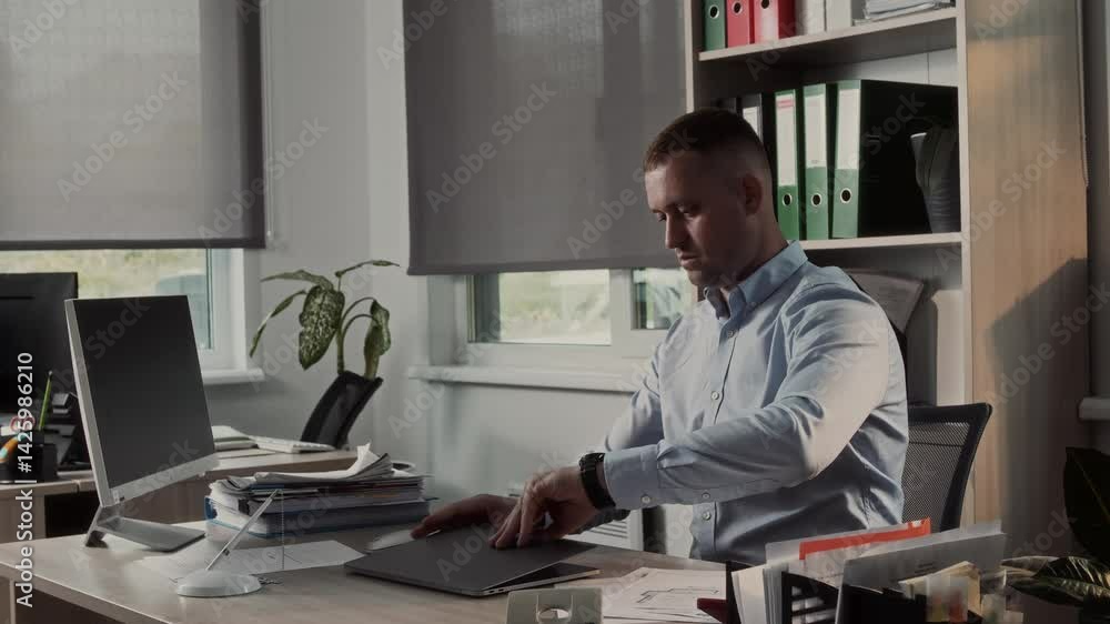 Professional office worker sits down at a desk with a compact laptop, checks the time with a wristwatch and gets to work on the computer Professional office worker sits down at a desk with a compact laptop, checks the time with a wristwatch and gets to work on the computer